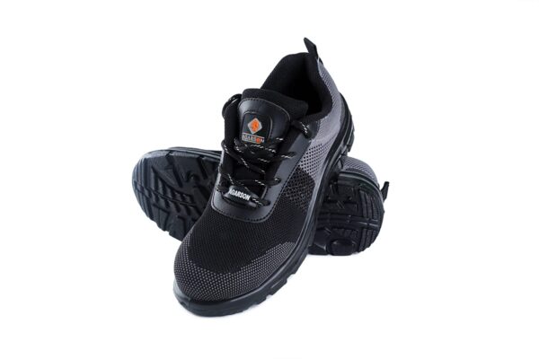 A pair of black and dark grey Agarson hyryder safety shoe with mesh detailing. The shoes have thick, black rubber soles, lace-up closures, pull tabs on the heels, and a small logo visible on the tongues featuring an orange and black design. These safety shoes are positioned side by side.